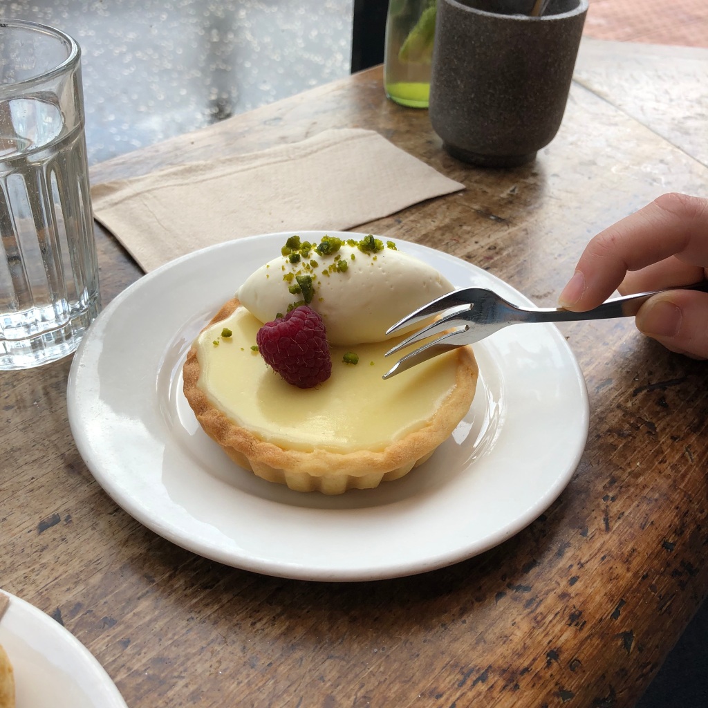 Image of white chocolate tart with singular raspberry and scoop of cream.